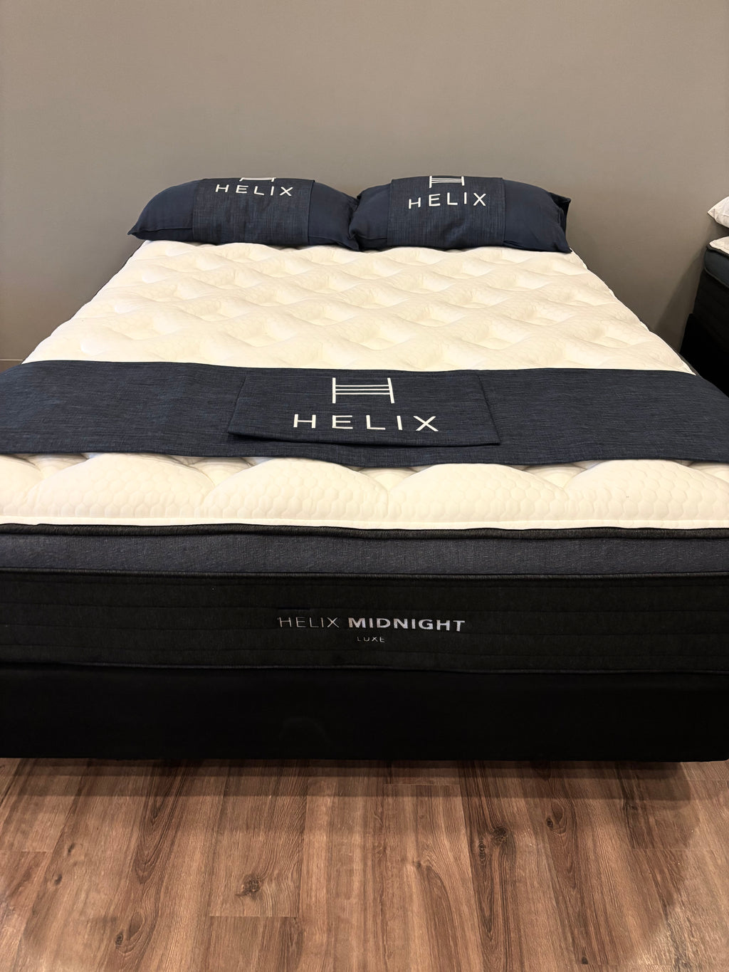 Helix mattress with bedding on a wooden floor against a gray wall