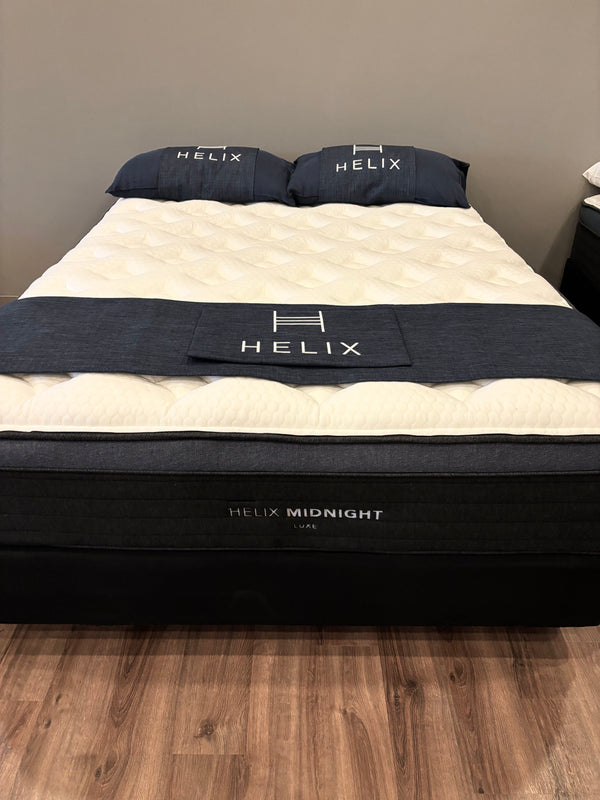 Helix mattress with bedding on a wooden floor against a gray wall